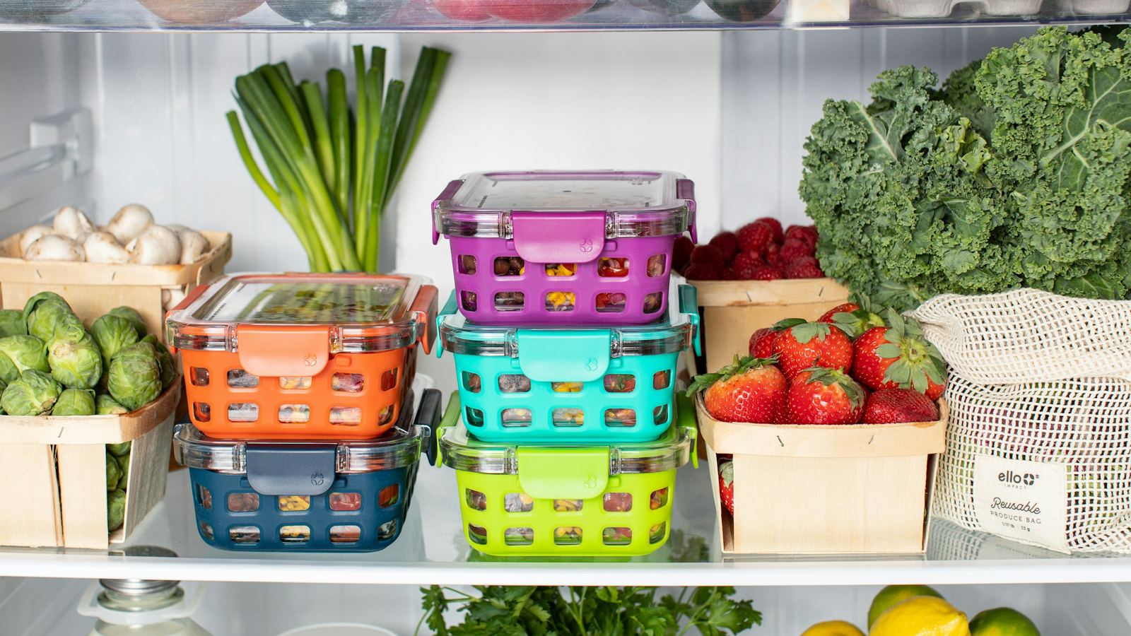 Fridge shelves with spring onions, kale, strawberries and stacked food boxes